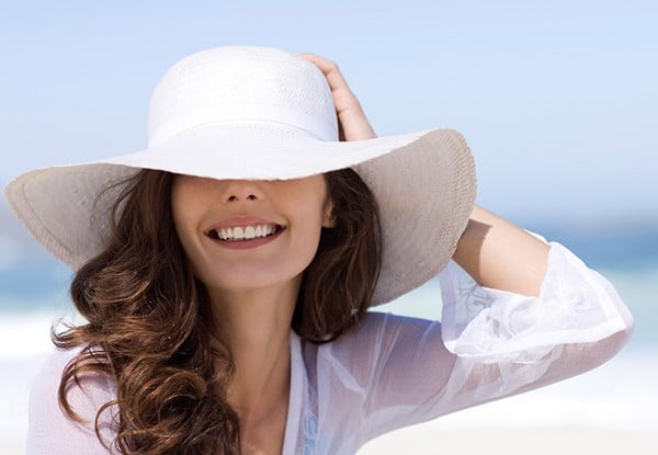 Young Brunette Woman In A White Blouse And Hat On The Beach